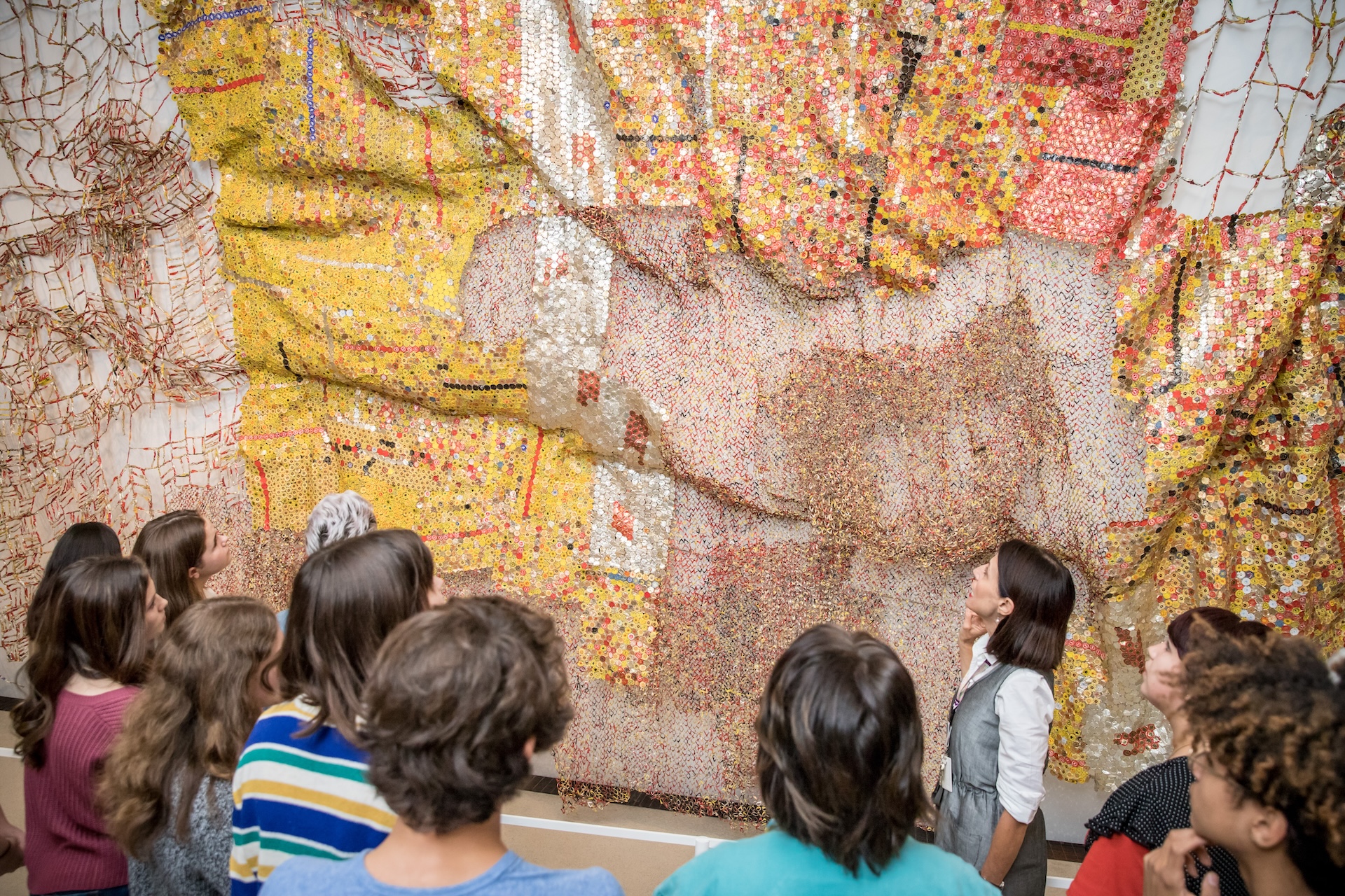 A group of people viewing a large mosaic artwork with various colors, including yellow, orange, white, and pink.