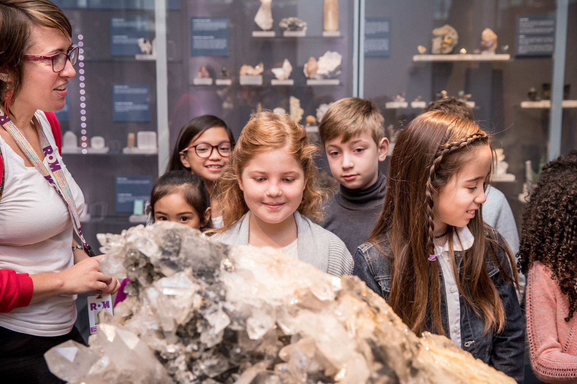 A group of children and an adult are gathered around a large mineral or crystal display in a museum exhibit.