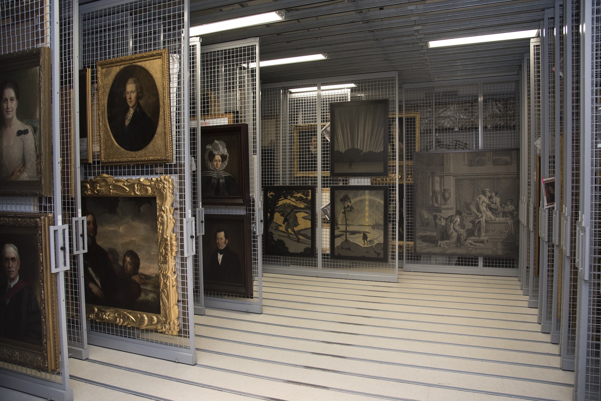 A storage area with art pieces on racks including framed paintings and portraits in a museum setting.