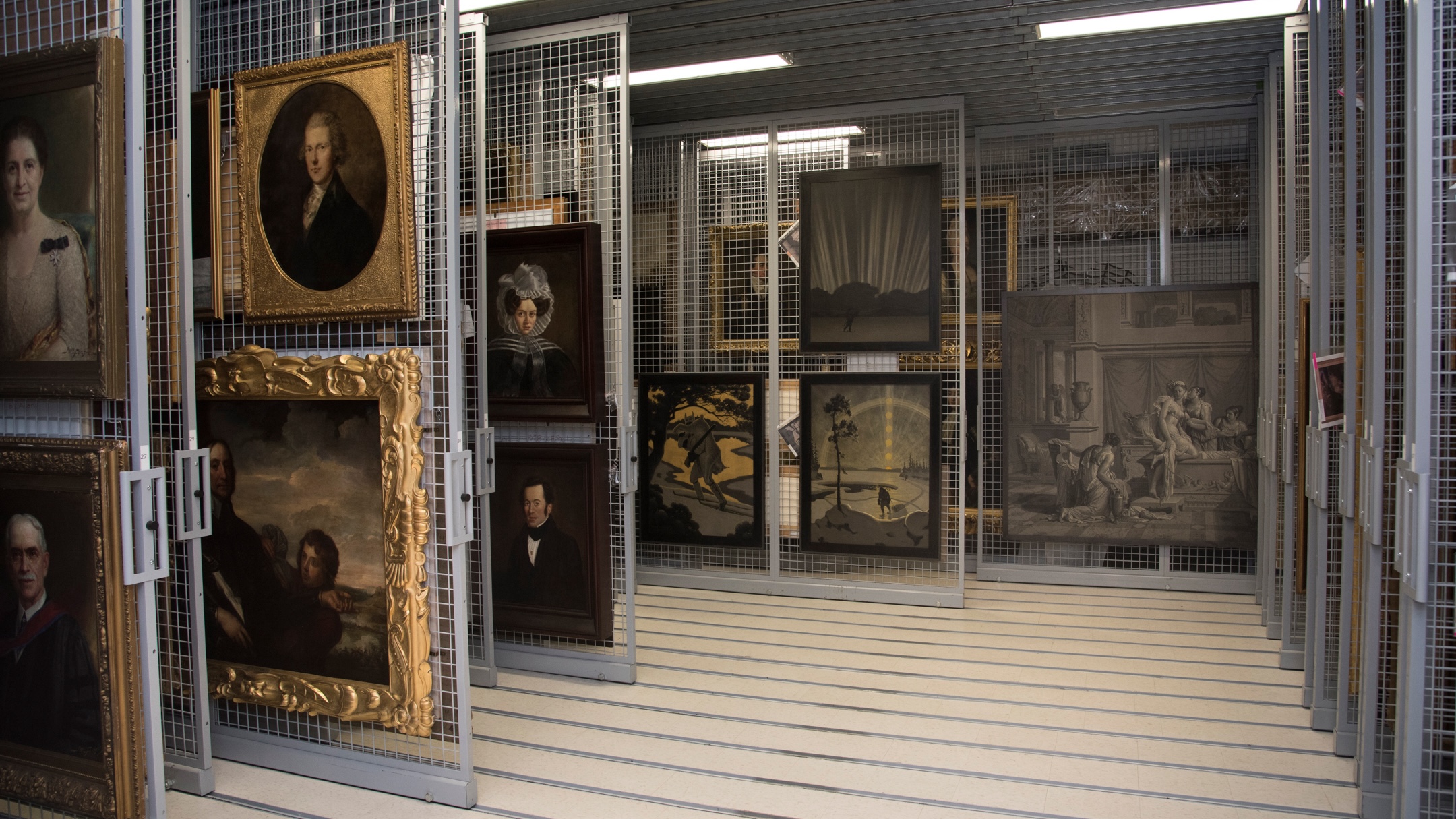 Interior view of a museum storage area with artworks and paintings on metal racks.