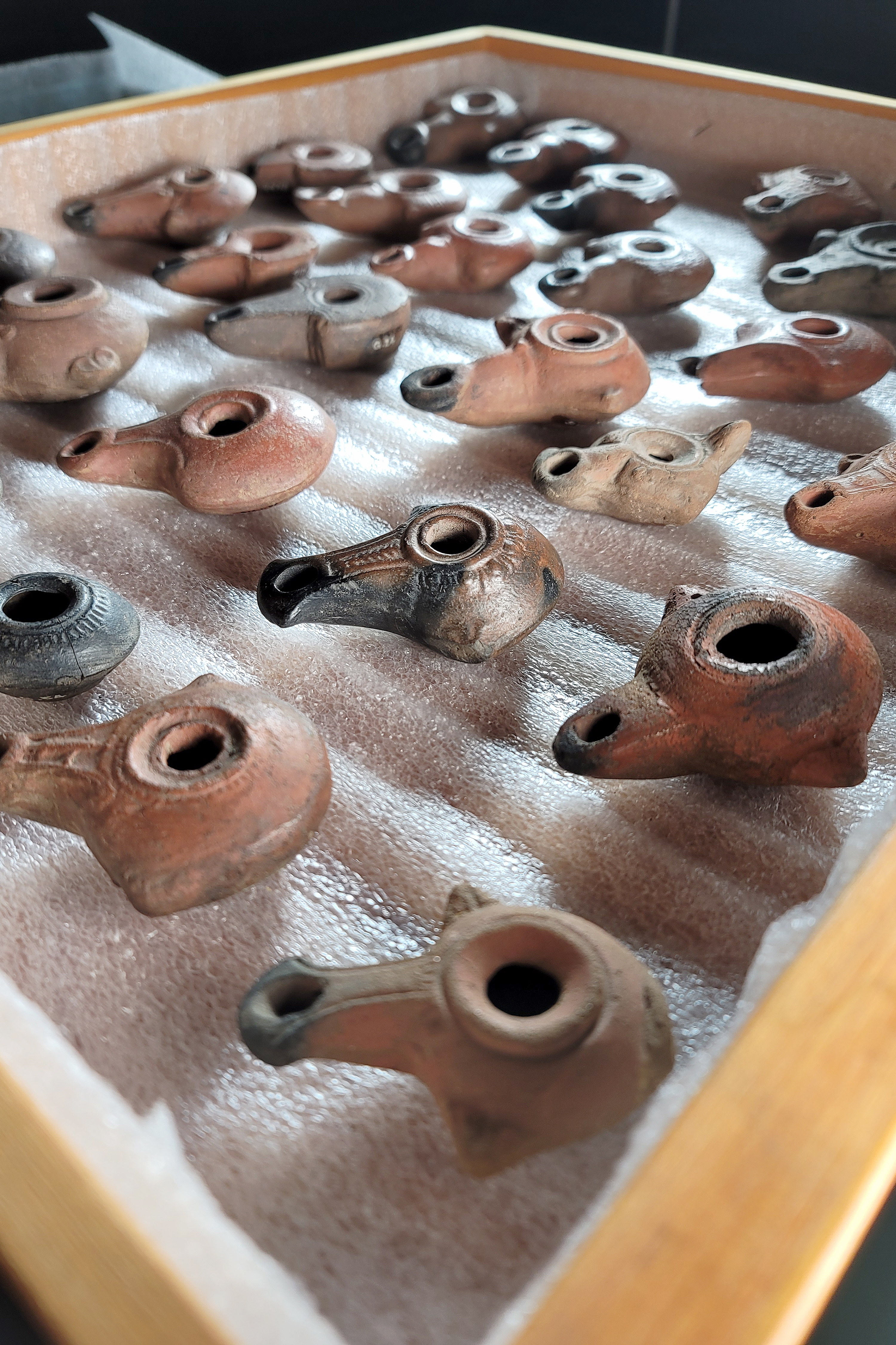 Tray displaying an assortment of small, ancient ceramic oil lamps arranged in rows.