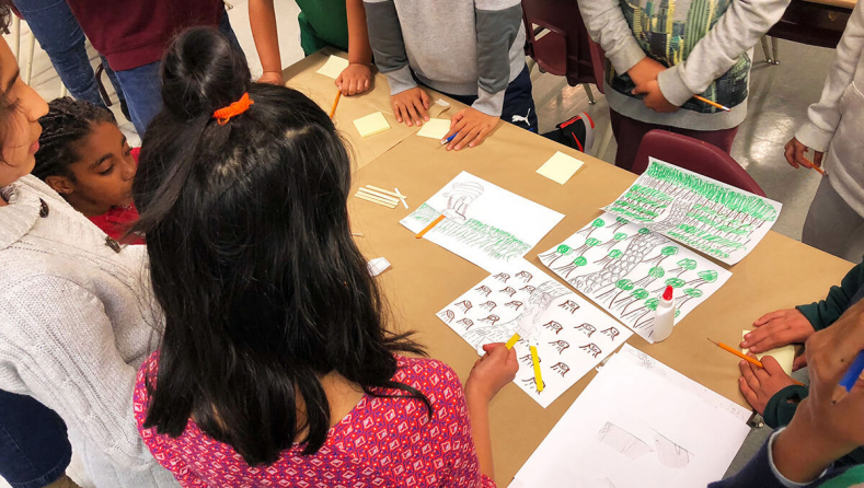 Children's hands and arms around a table with sheets of paper showing different insects and animals.