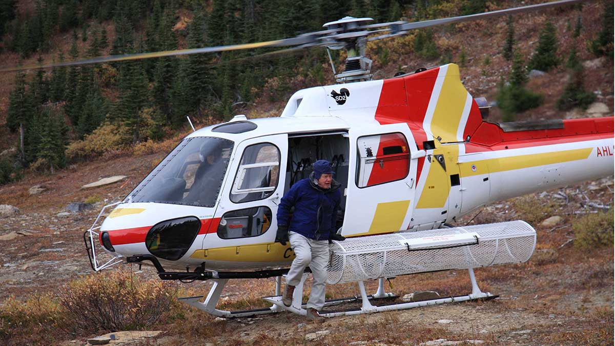 White helicopter with red and yellow stripes parked on grass, with one person standing beside it.