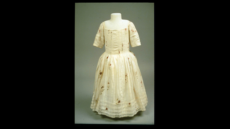 Cream-colored dress with elbow-length sleeves and a full skirt decorated with a subtle floral pattern.