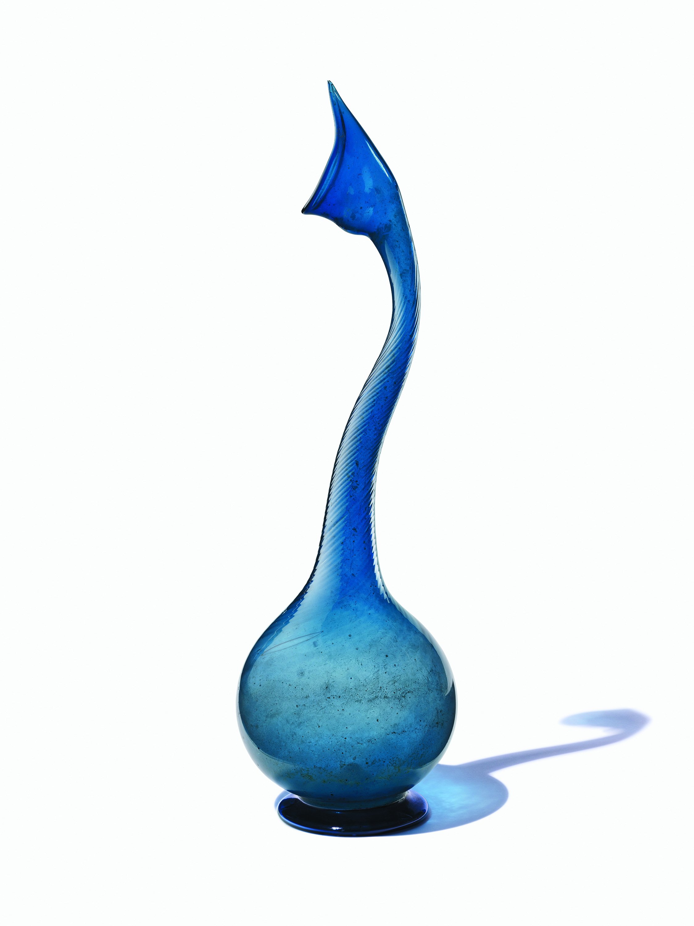 Grand vase élancé en verre bleu avec un col incurvé et une base bulbeuse qui projette une ombre.