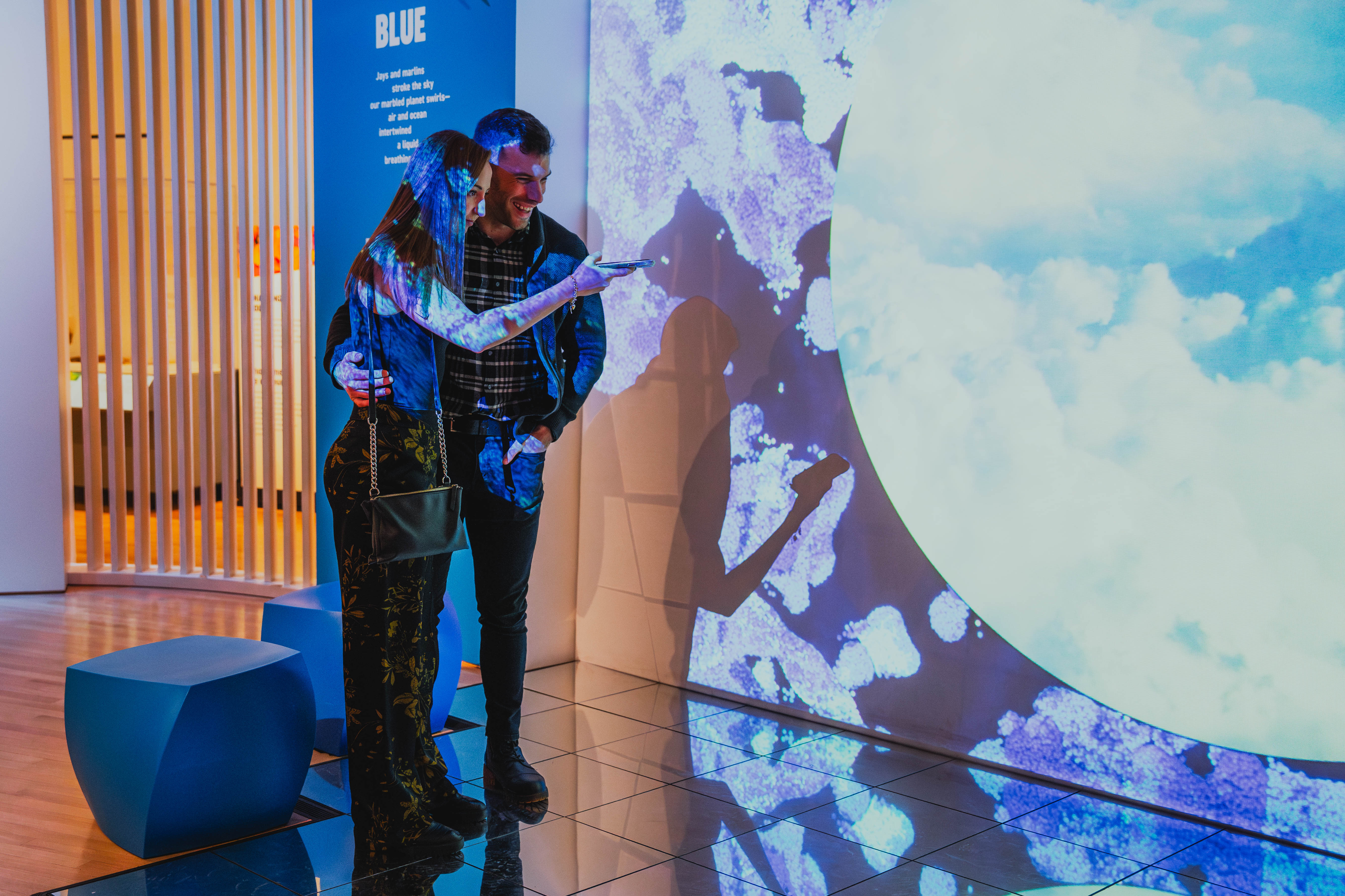 Two men interact with illuminated blue and white digital projections on a curved wall in a modern indoor space.