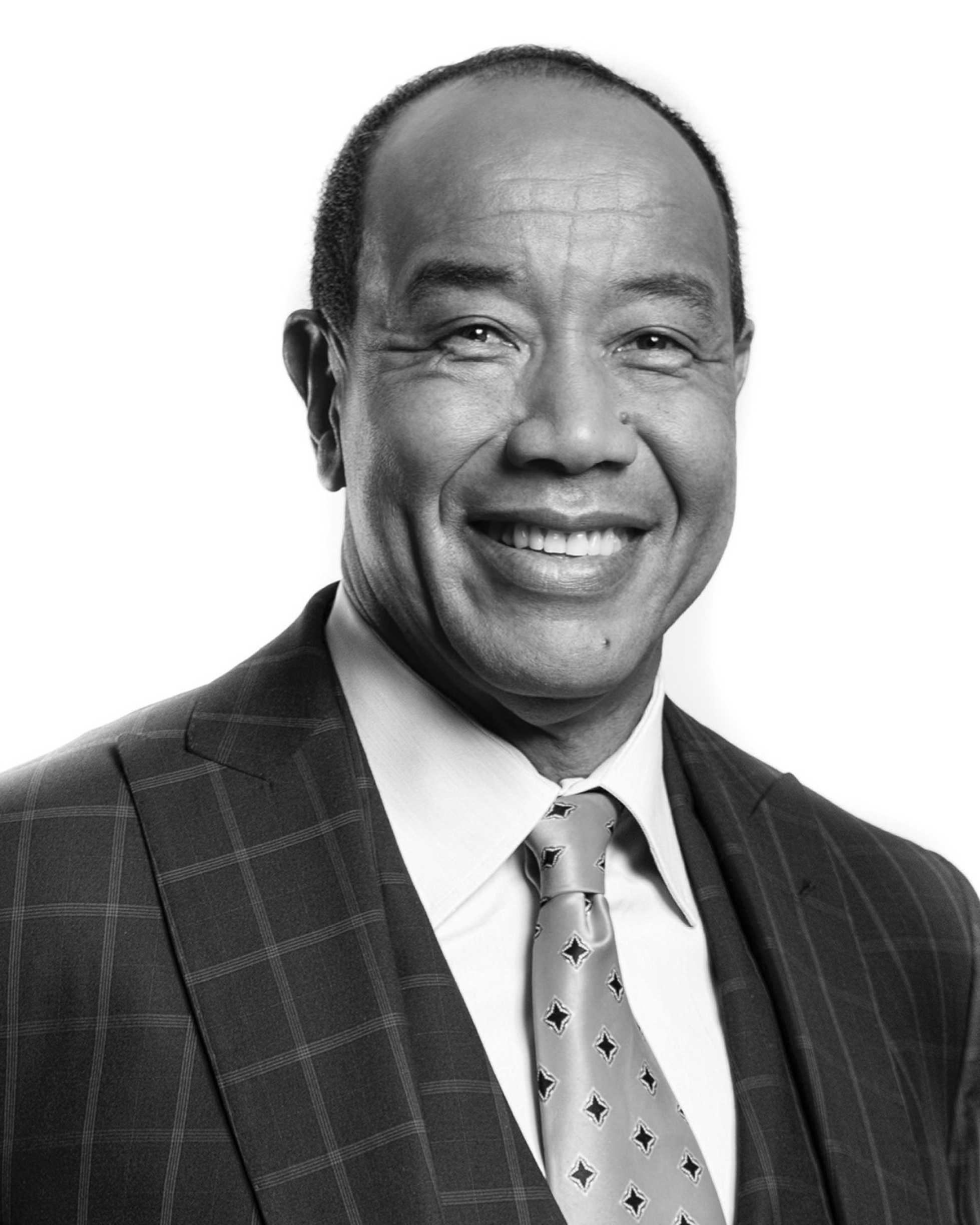 Portrait of a bald man smiling, wearing a dark checkered suit jacket, white shirt, and polka dot tie.