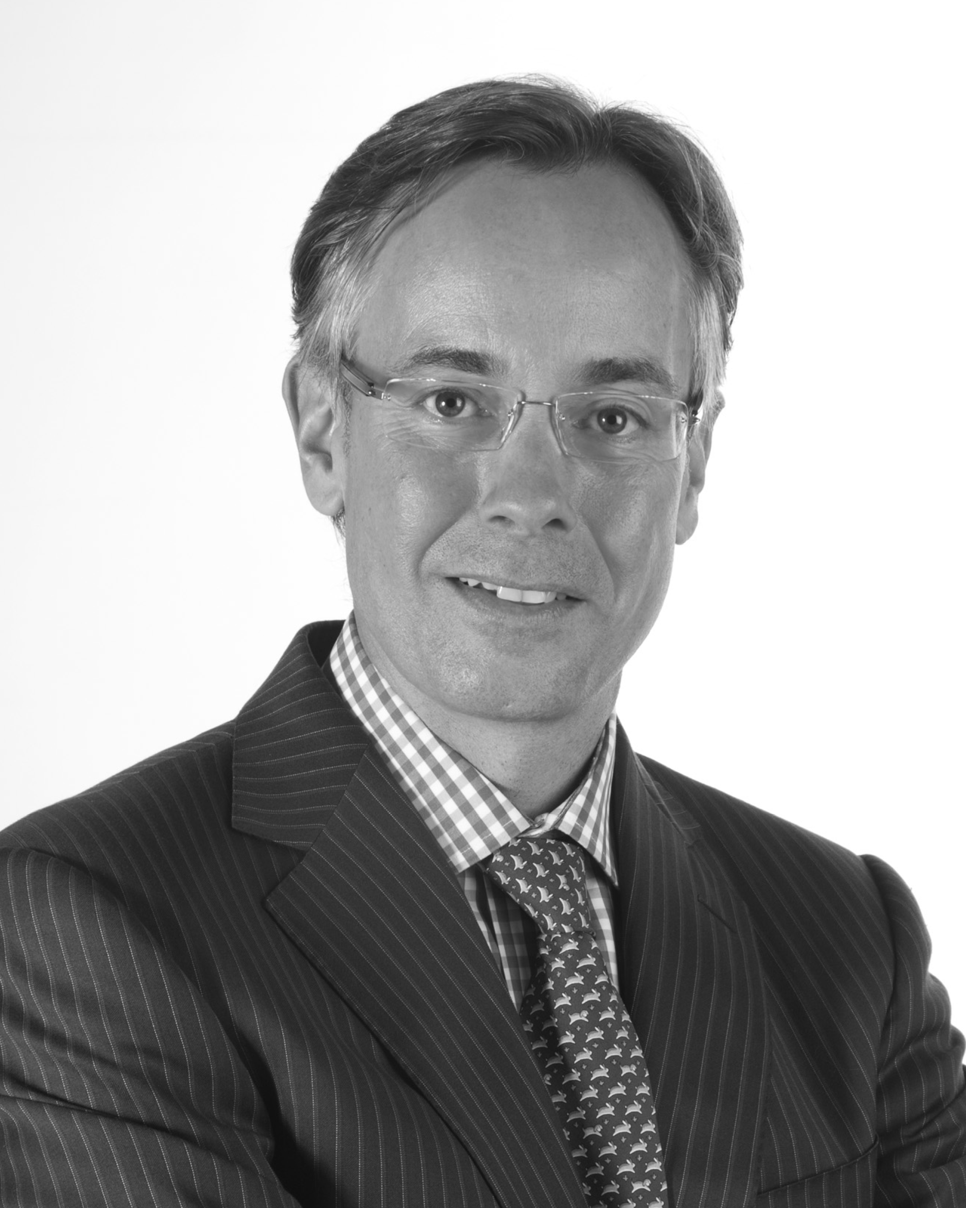 Portrait of a man wearing glasses, a dark pinstripe suit, a checkered shirt, and a patterned tie, smiling.