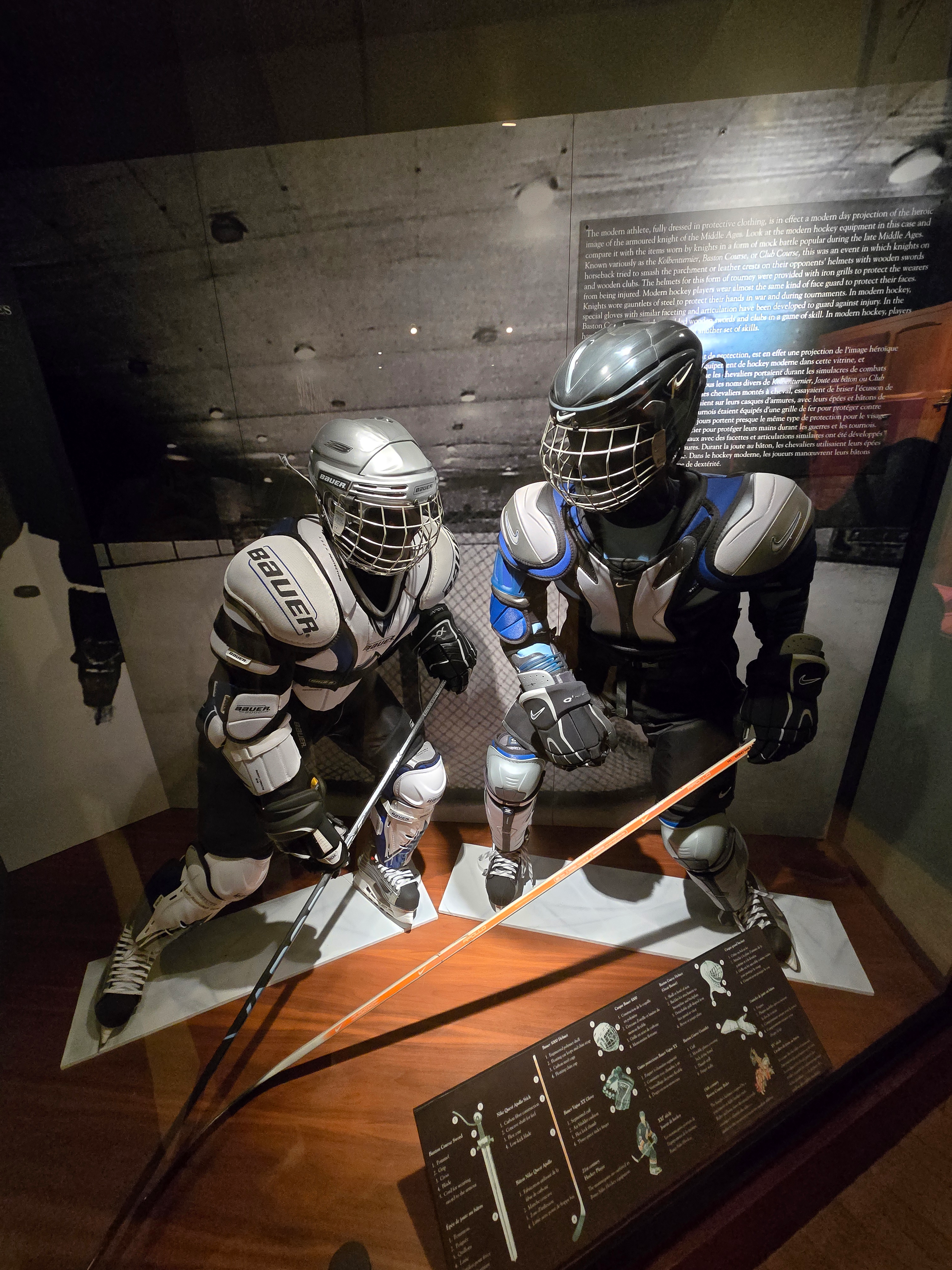 Deux mannequins vêtus d'équipements de hockey Bauer, y compris des épaulettes, des tibias, des gants, des patins et des casques. Les deux mannequins tiennent des crosses de hockey et prennent des poses dynamiques.