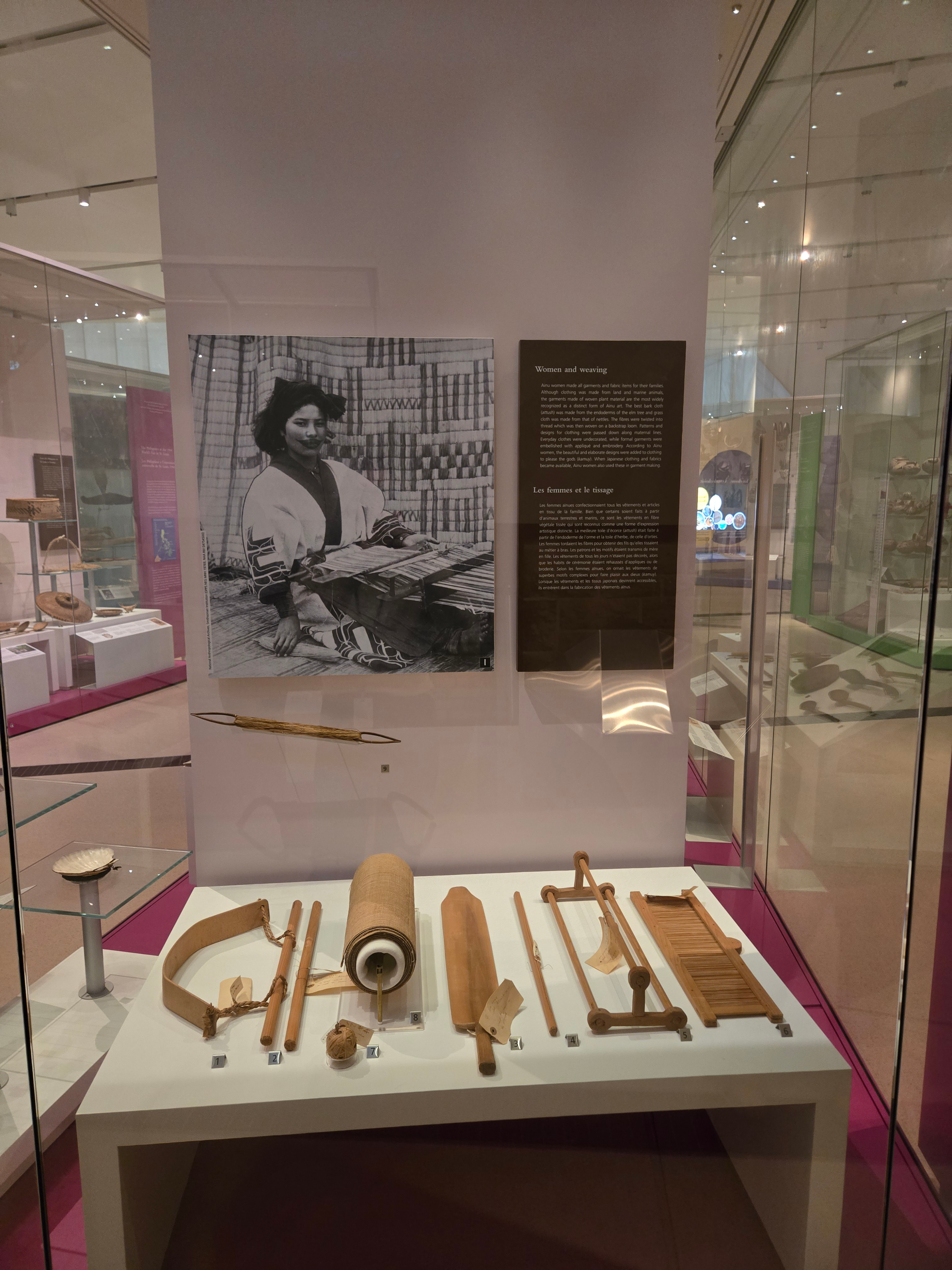 Dans la galerie d'un musée, une vitrine présente divers outils de tissage en bois.