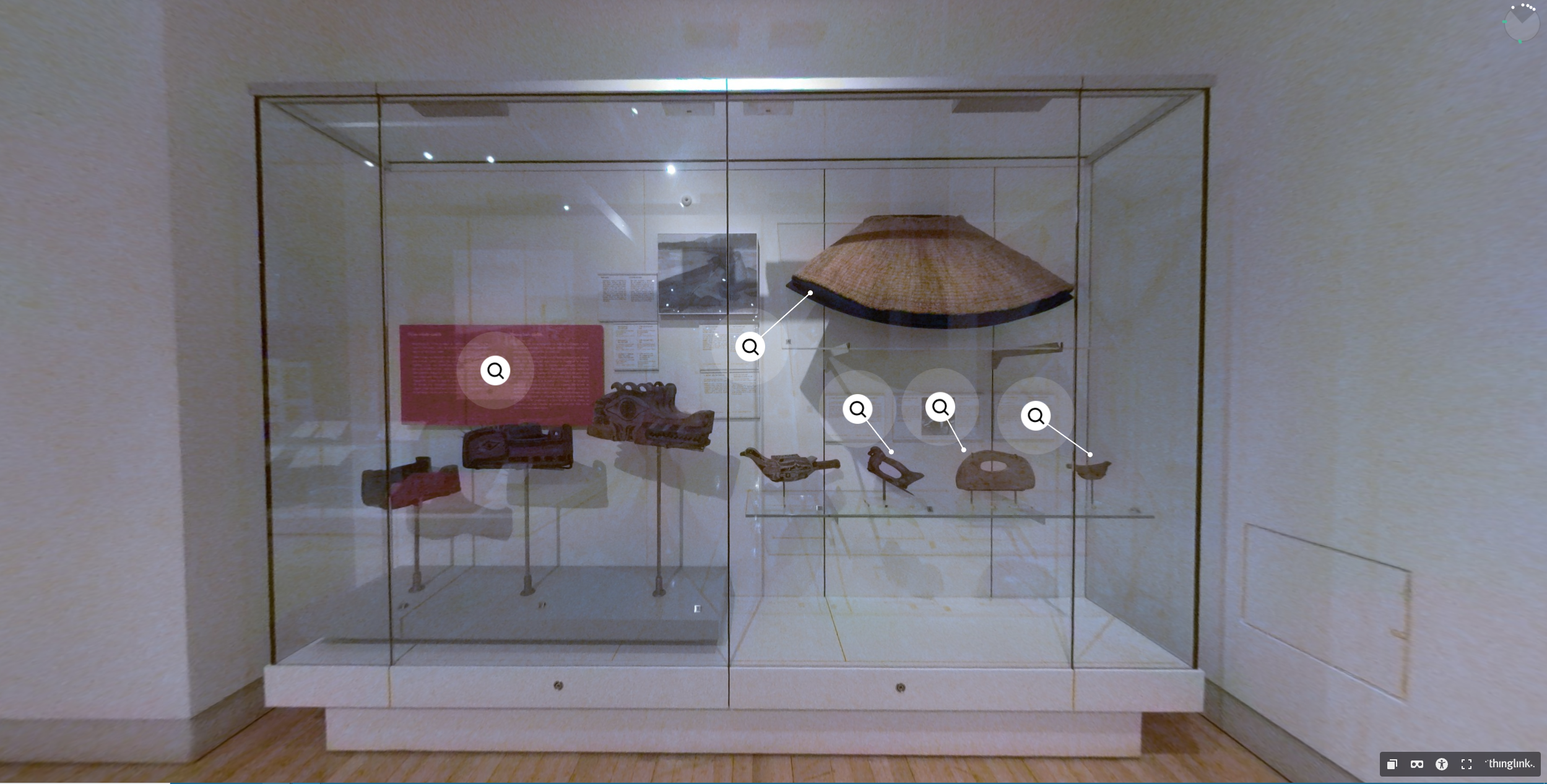 A case in a museum displaying many belongings made from cedar, including a cape, masks, and several tools.