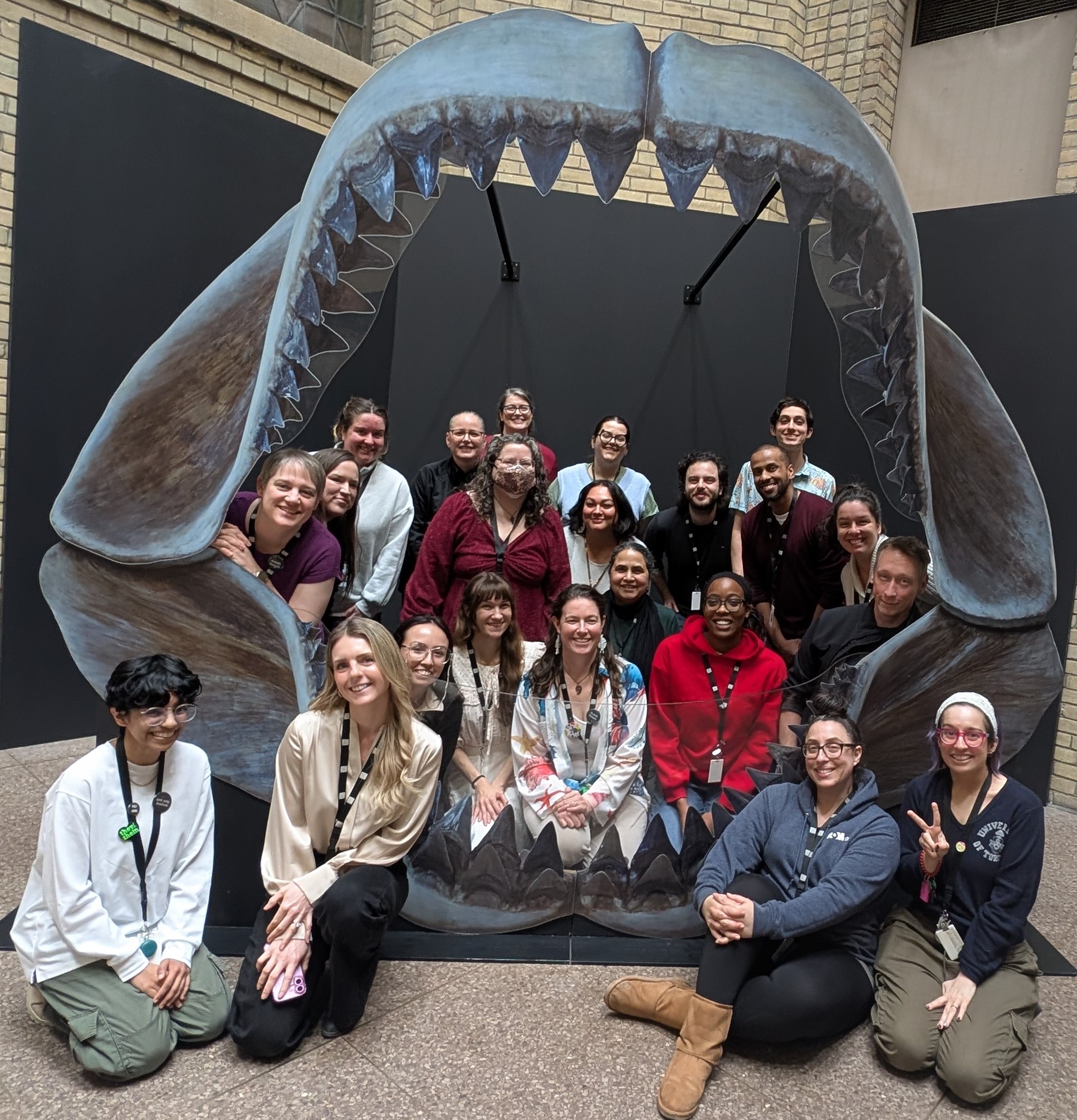 A group of smiling educators stands in a cutout of a shark's mouth