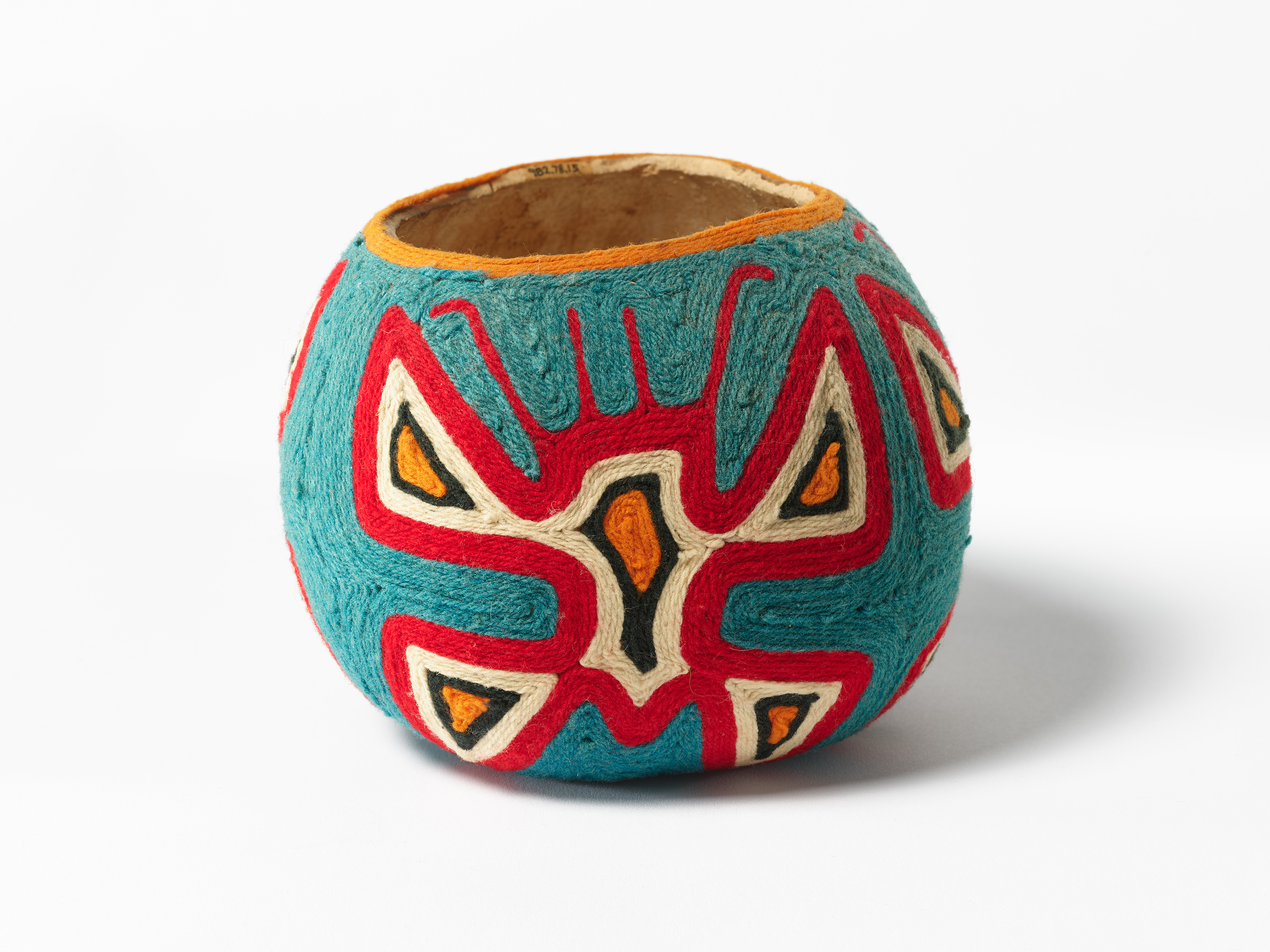 Small rounded vessel covered in blue fabric with red, white, black, and yellow decorative geometric patterns.