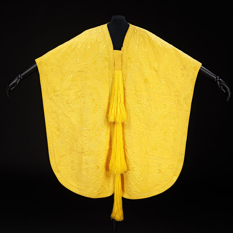 Yellow poncho with floral embroidery and three long tassels hanging down the front.