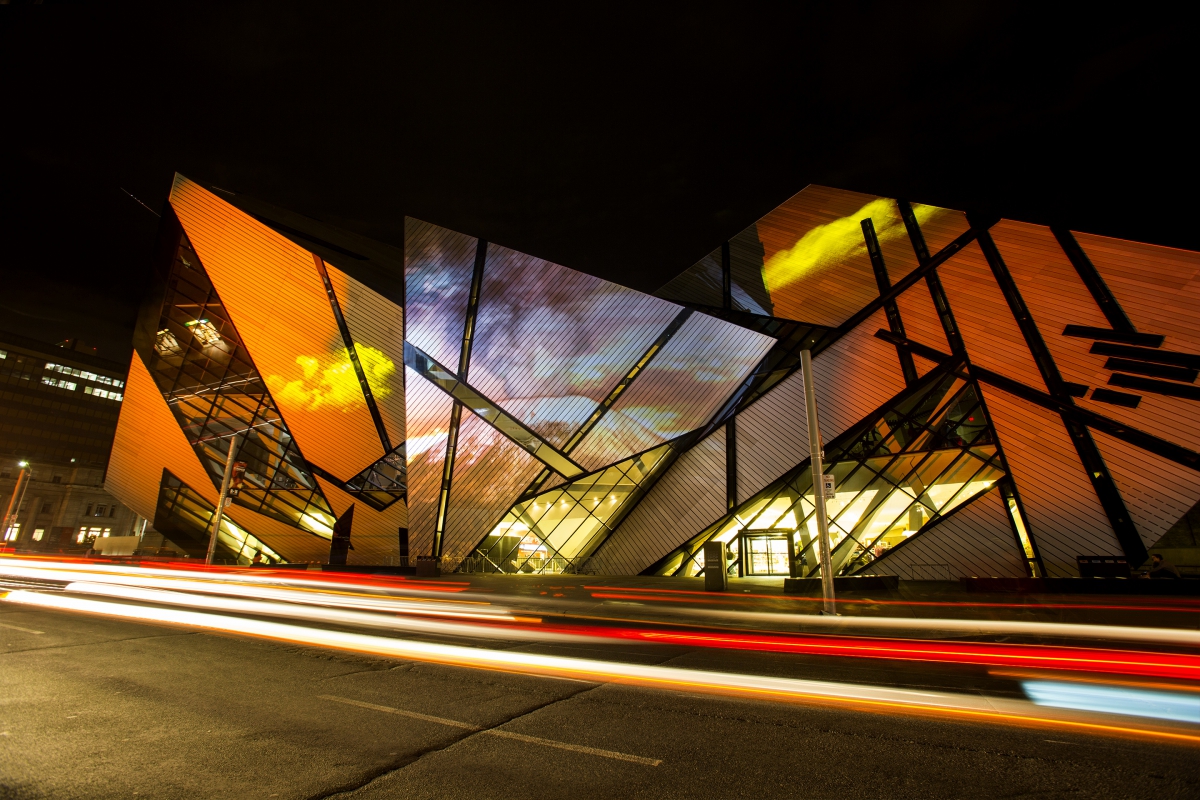 Night view of the Royal Ontario Museum's Michael Lee-Chin Crystal architectural facade illuminated with orange and yellow lights.