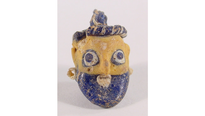 Small ancient mask with a yellow face, blue beard, and detailed black and blue headpiece.