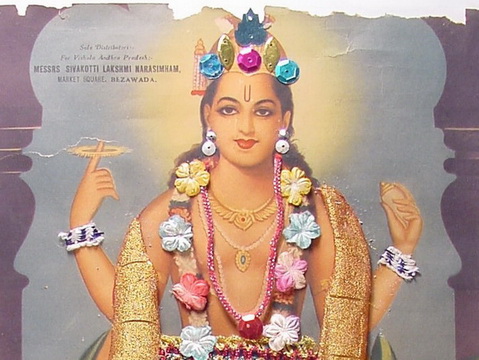 Goddess adorned with colorful flowers and jewelry, holding a pink lotus flower in her right hand and a ring in her left hand.
