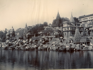 Historic black-and-white photograph of riverfront buildings and temples with spires reflecting in the water.