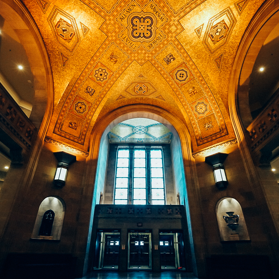 Interior view of a grand arched ceiling with intricate gold decorations and a large window above an entrance with three doorways.