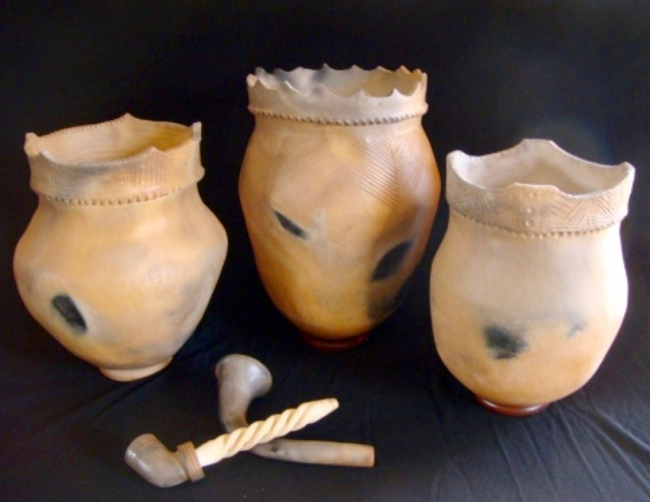 Three ancient clay pots with scalloped rims and black smudges, accompanied by three carved bone or ivory tools.