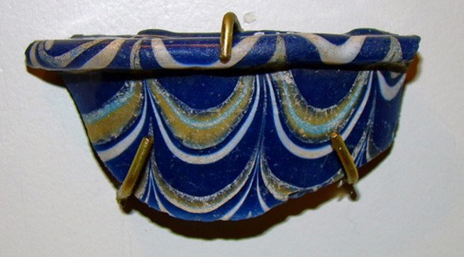 Blue and white ceramic vessel with gold accents in a scalloped pattern, held by three gold rings.