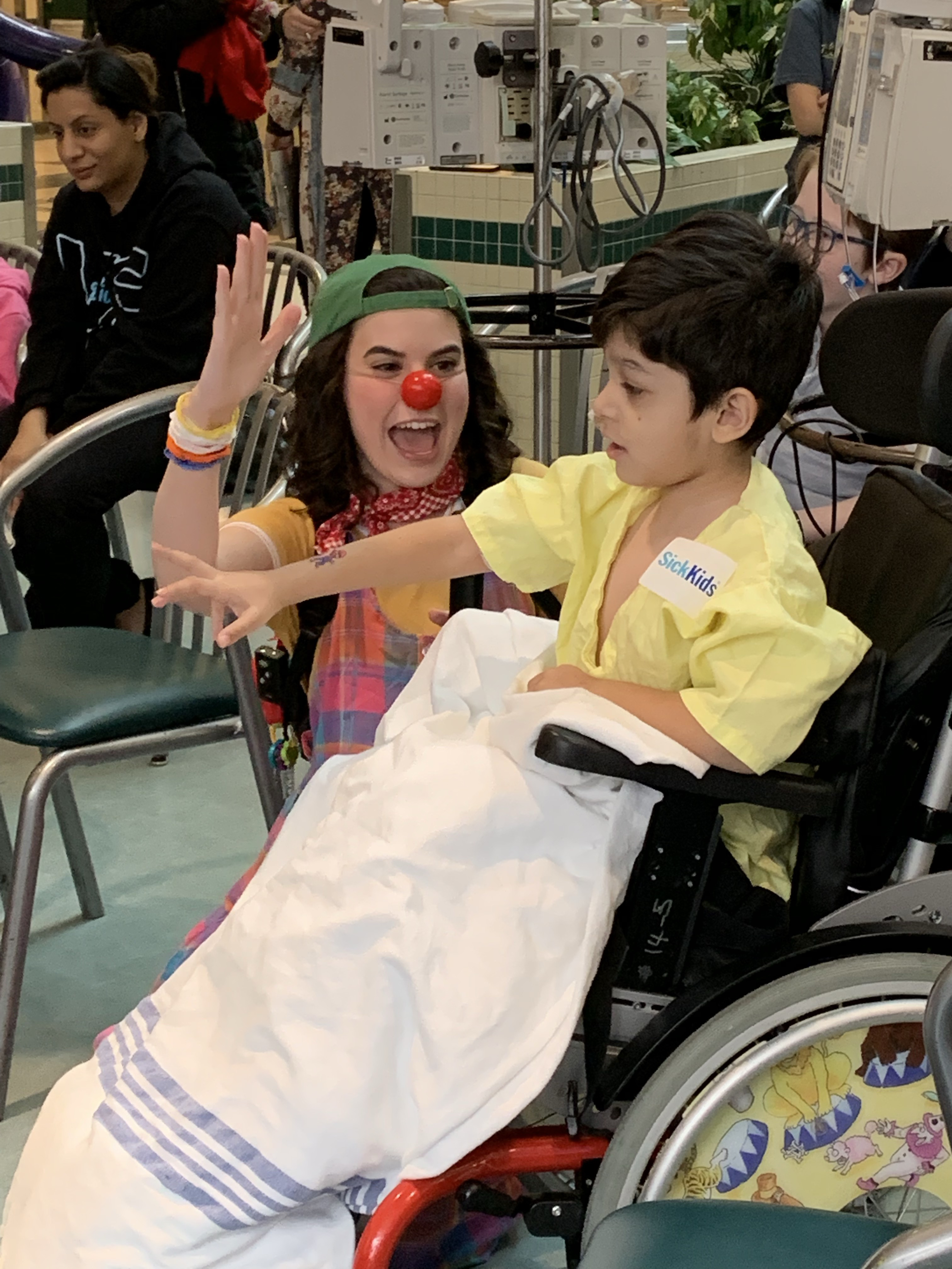 A performer with face paint gives a high-five to a child in a wheelchair covered with a blanket.