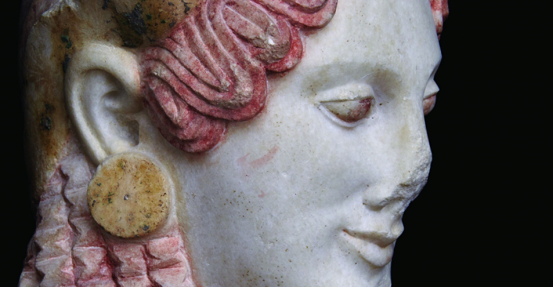 Gros plan du visage d'une sculpture en marbre avec des boucles de cheveux roses détaillées et une grande boucle d'oreille circulaire.