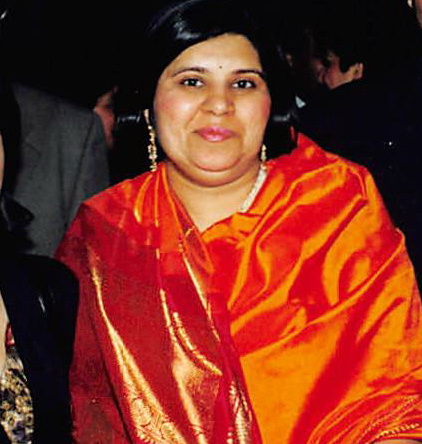 Woman wearing a red-orange silk shawl with gold jewelry in a dimly lit setting.