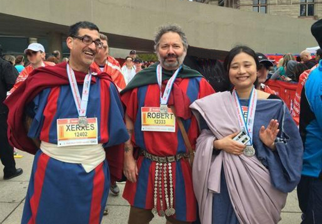 Three people dressed in Roman soldier costumes stand together wearing medals on blue ribbons around their necks.