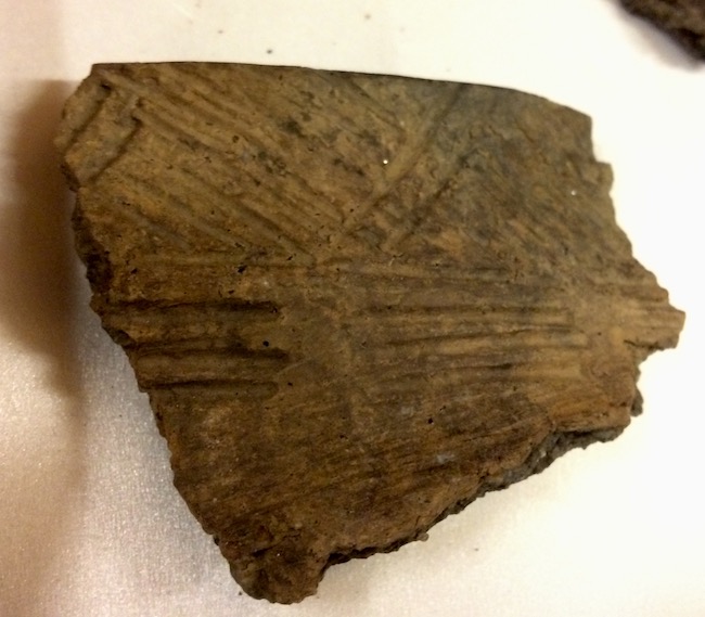 Fragment of brown pottery embossed with a pattern of parallel diagonal lines and parallel grooves.