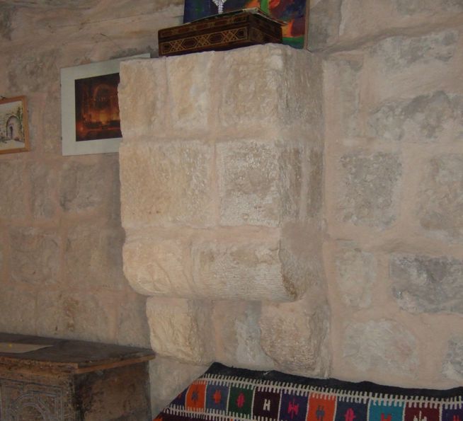 Stone medieval fireplace set in a stone wall above a colorful woven rug and beside a wooden chest.