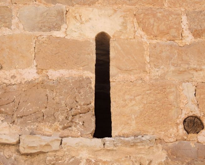 Narrow vertical slit window in a weathered stone wall.