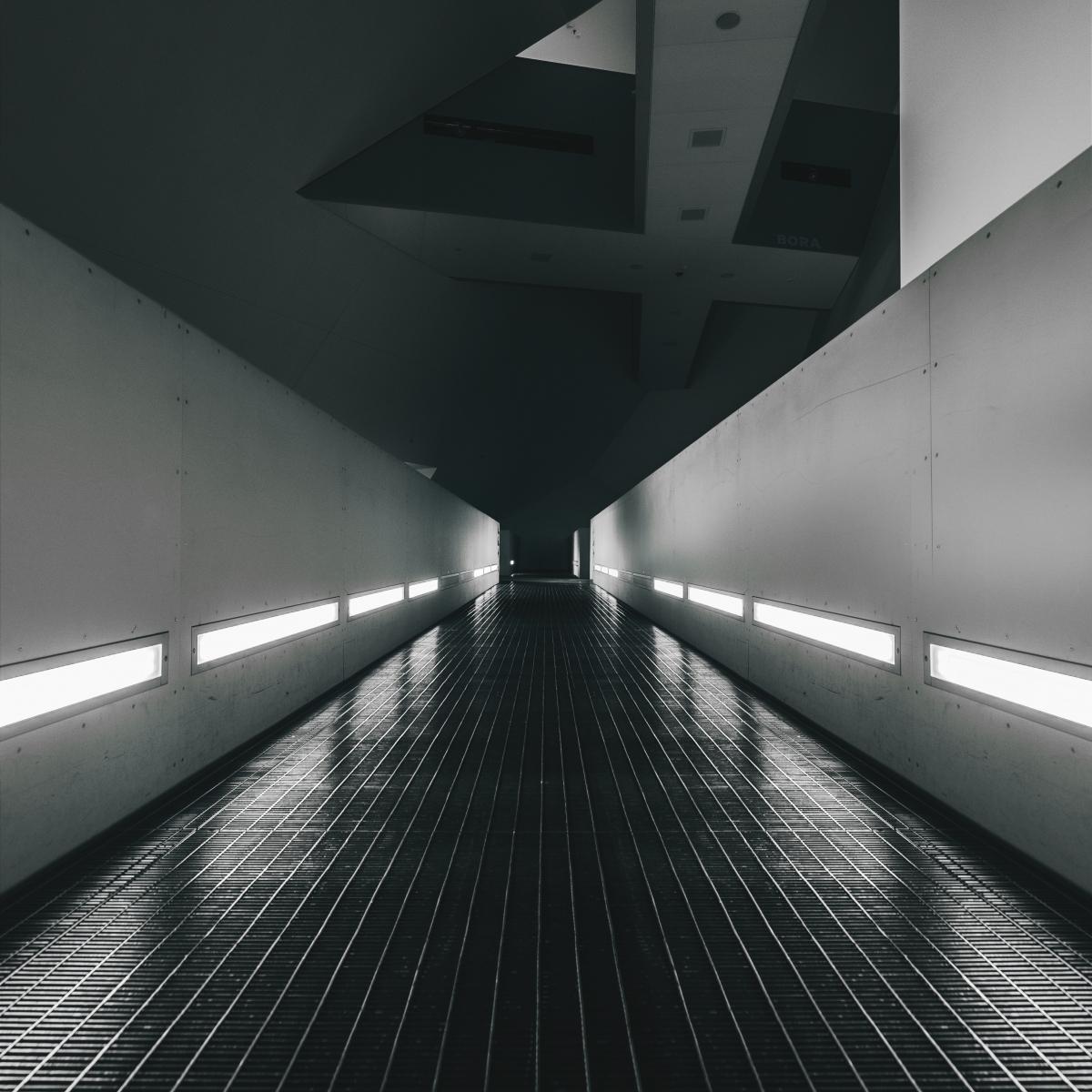Long corridor with modern gray walls, linear lights, and a tiled floor, converging at a vanishing point.
