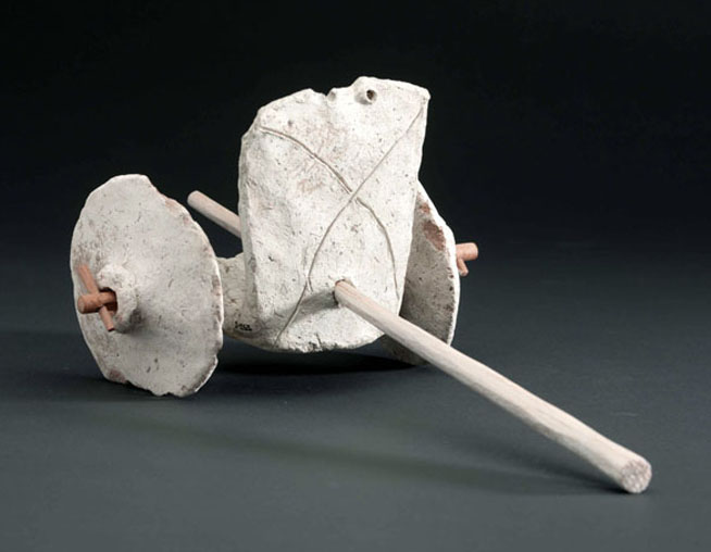 A small ancient ceramic artifact with a cylindrical body, a long spout, and a circular base against a black background.