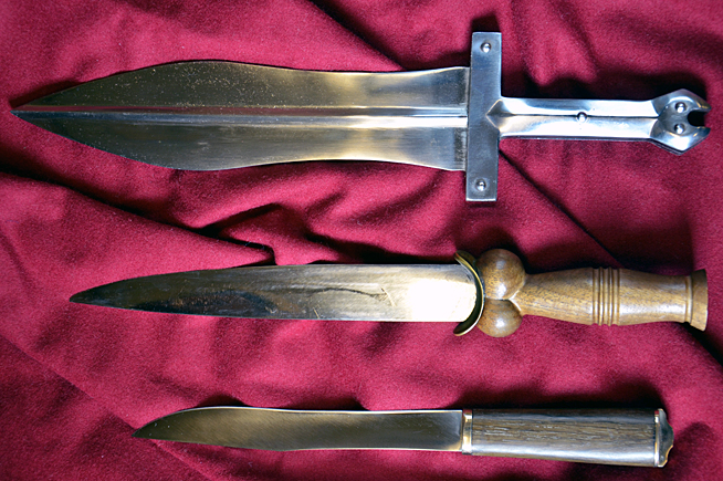 Three historical daggers with different blade shapes and handle designs displayed on a red fabric background.