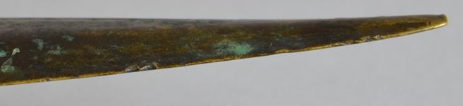 Close-up of a bronze, slightly curved, pointed artifact with visible verdigris corrosion.