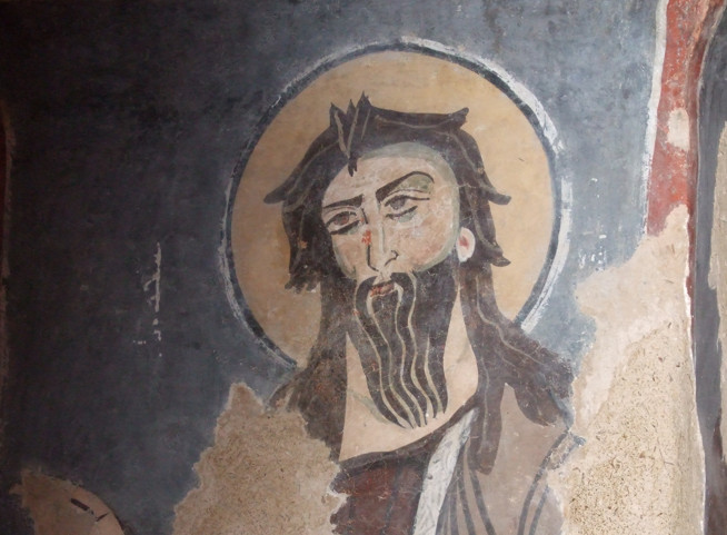 Byzantine-style religious fresco of a bearded man with a halo holding a book or scroll.