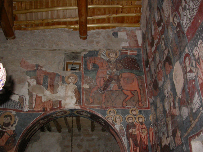 Interior walls covered with ancient murals depicting various human figures and scenes in earthy red and brown tones.