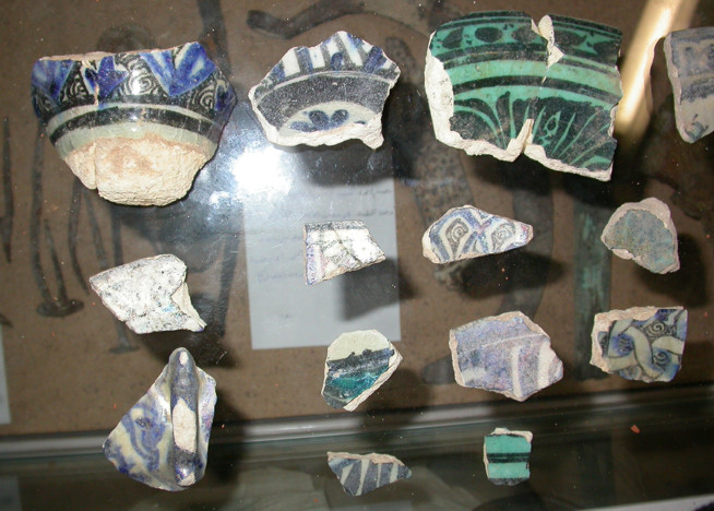 Broken ceramic fragments with blue, green, and brown decorative patterns displayed on a reflective surface.