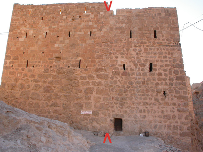 Large stone fortress wall with small rectangular openings and one small dark entrance near the base.