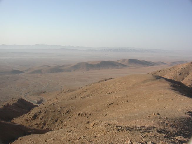 Arid, rocky desert landscape with low hills under a hazy, pale blue sky.