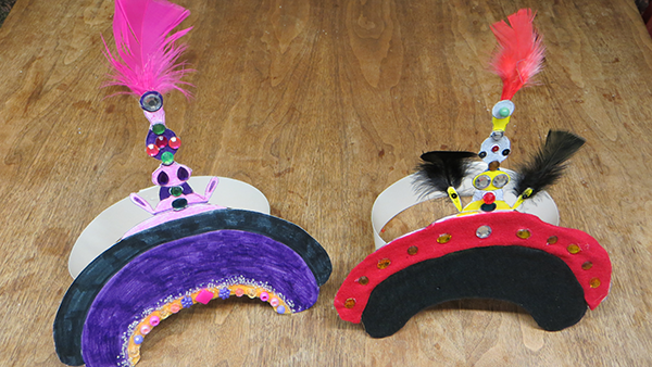 Two colorful feathered headdresses with beads, one purple and one red, placed on a wooden surface.