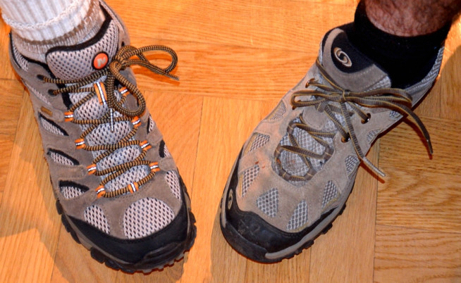 Two worn gray hiking shoes with brown laces on a wooden floor.