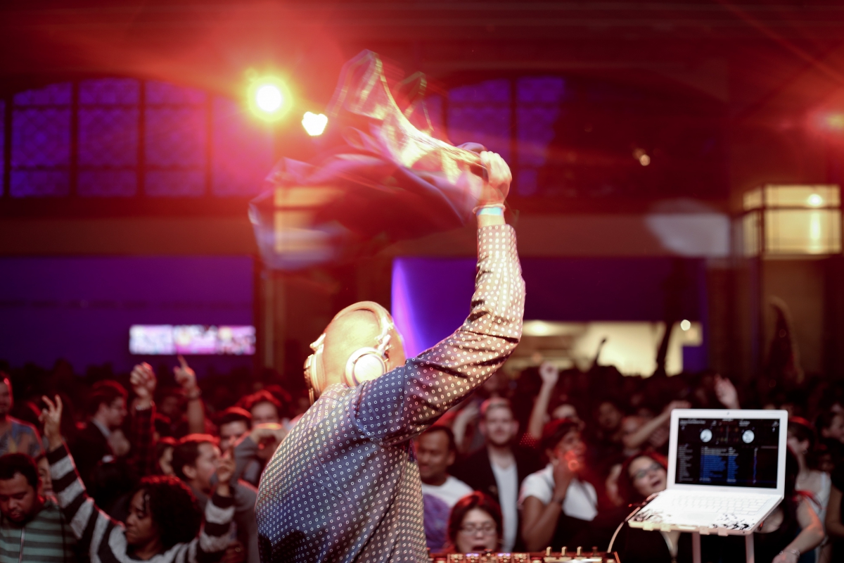 Man holding up a microphone in front of a crowd of cheering people in a dimly lit venue.