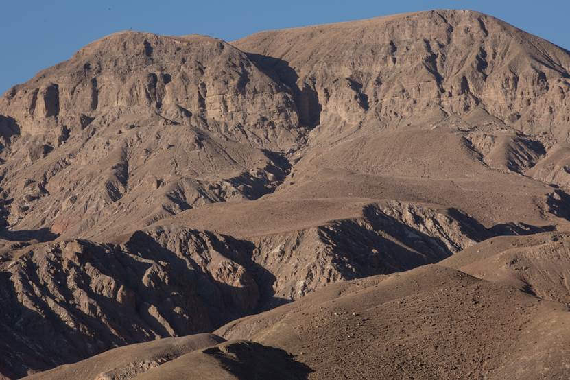 Arid, rocky mountain landscape with steep, barren slopes under a clear sky.