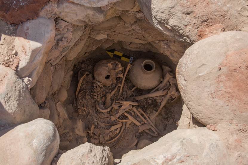 Skeleton remains curled inside a rocky burial pit alongside two large pottery vessels.