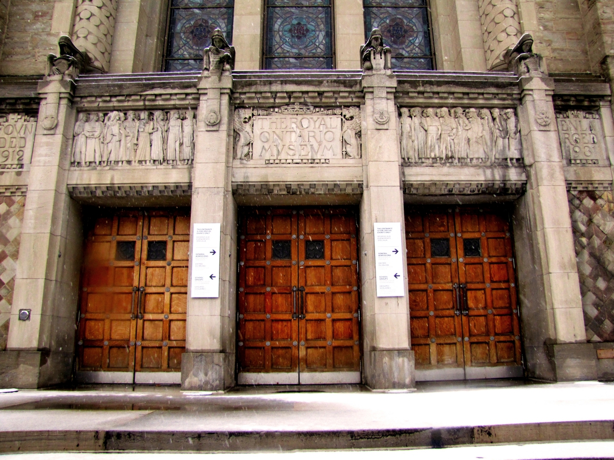 Three large wooden doors framed by stone columns and decorated stone panels above the entrance.