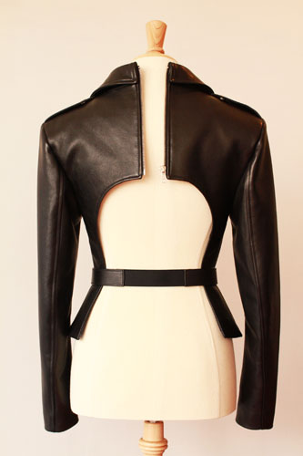 Back view of a cropped black leather jacket with a wide rectangular cutout on the back and a belt at the waist.