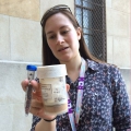 A woman with a lanyard looks at a labeled glass jar containing a brownish substance.