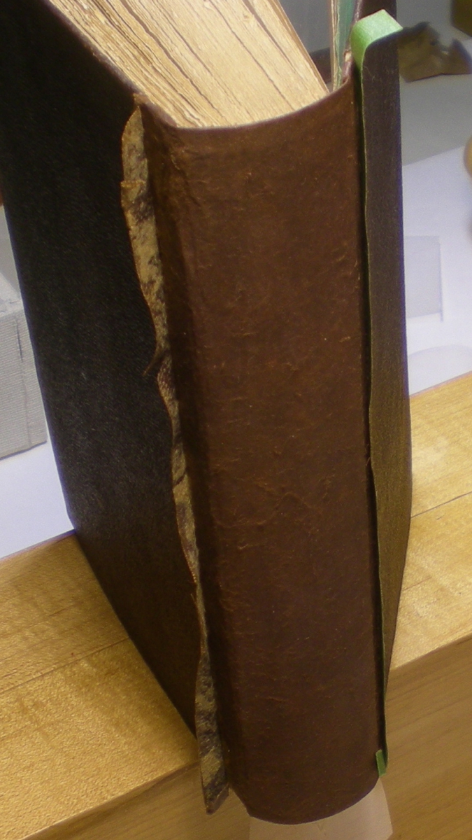 Close-up of the spine and part of the covers of a thick, old brown leather-bound book on a wooden surface.